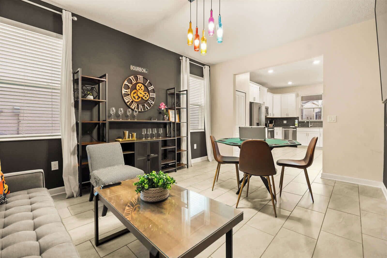 A modern living room with a sofa, a coffee table with a plant, a dining area with chairs and a table, and a kitchen in the background.