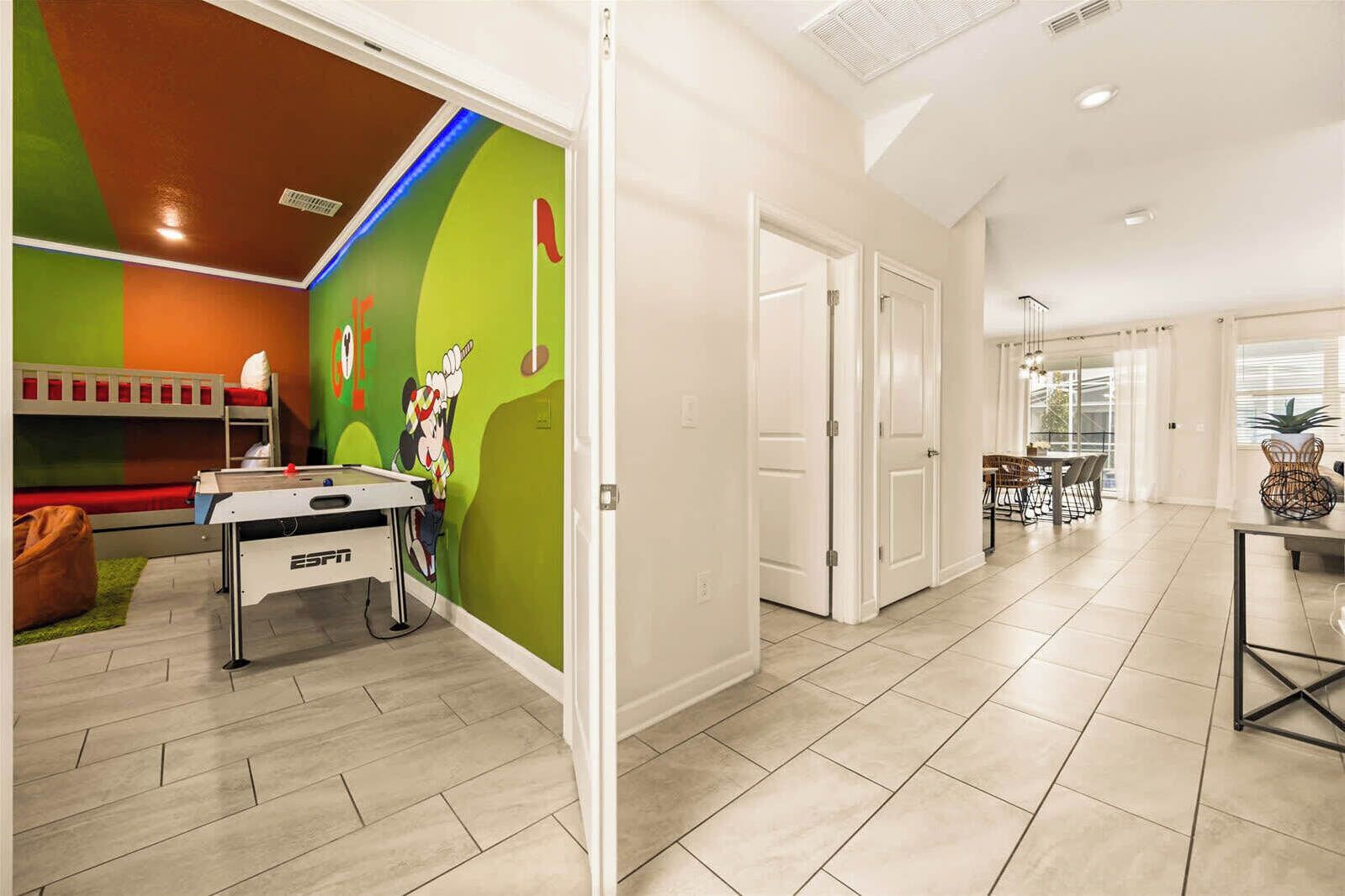 A modern living room with a pool table, a green wall with a cartoon character, and a dining area with a table and chairs.