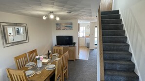 A dining area with a wooden table set for four, a television, and a staircase leading to another room.