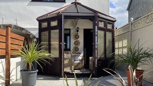 A conservatory with a wooden frame, a wicker sofa, and a potted plant.