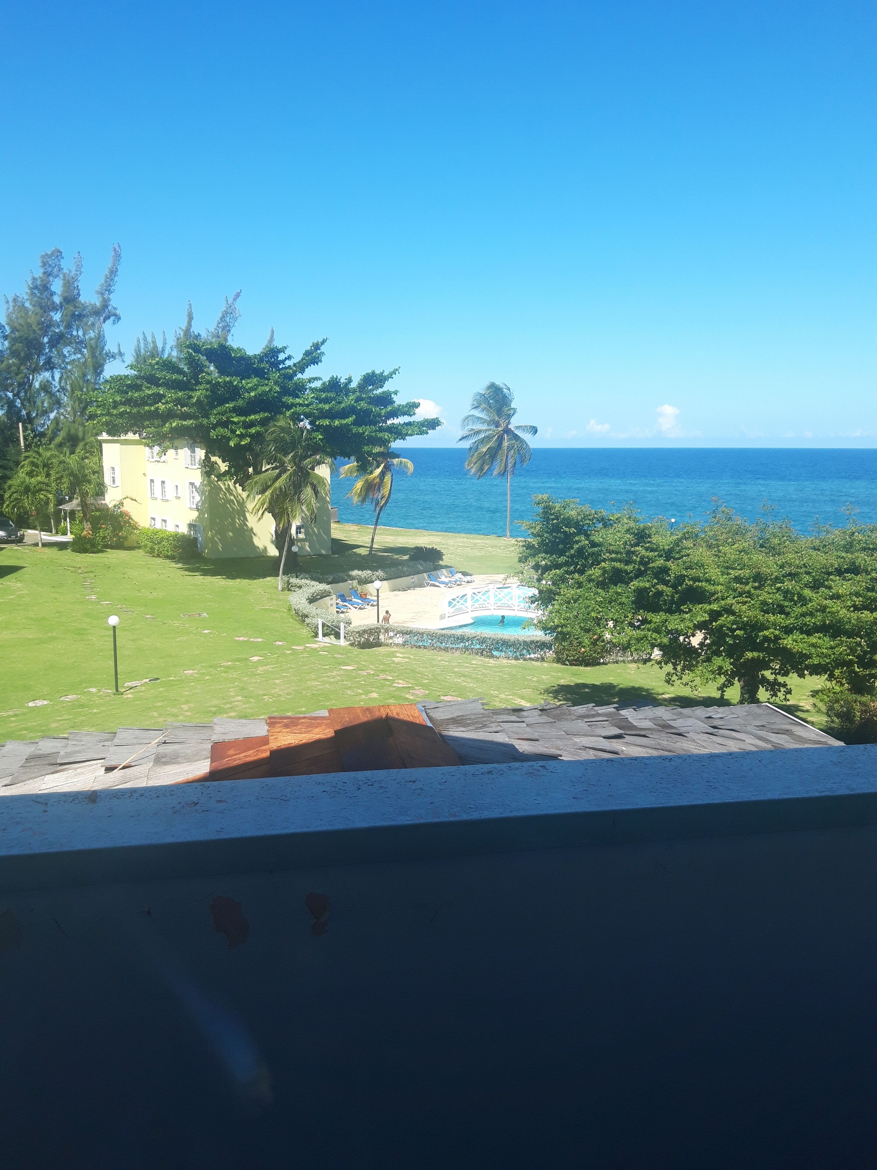 Vista de una zona de piscina con cielo azul despejado y el océano al fondo.