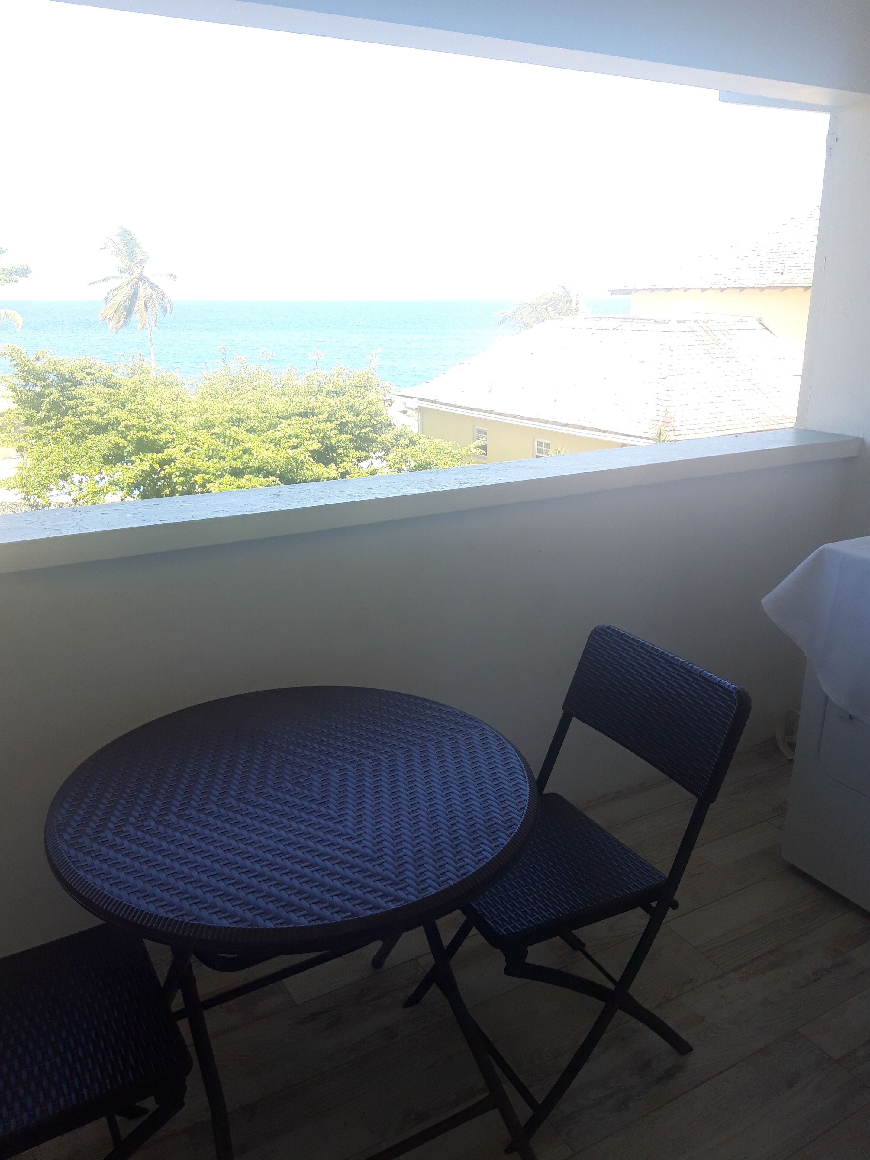 Un balcón con una mesa redonda y dos sillas, con vista a una playa y al océano.