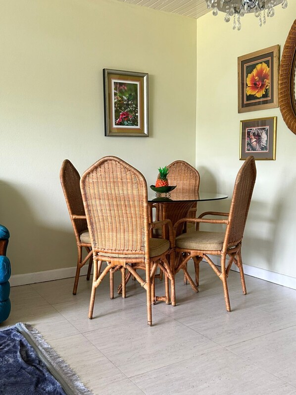 A dining area with wicker chairs and a glass table, framed pictures on the wall, and a chandelier. - Seapalms (Tower Isle)