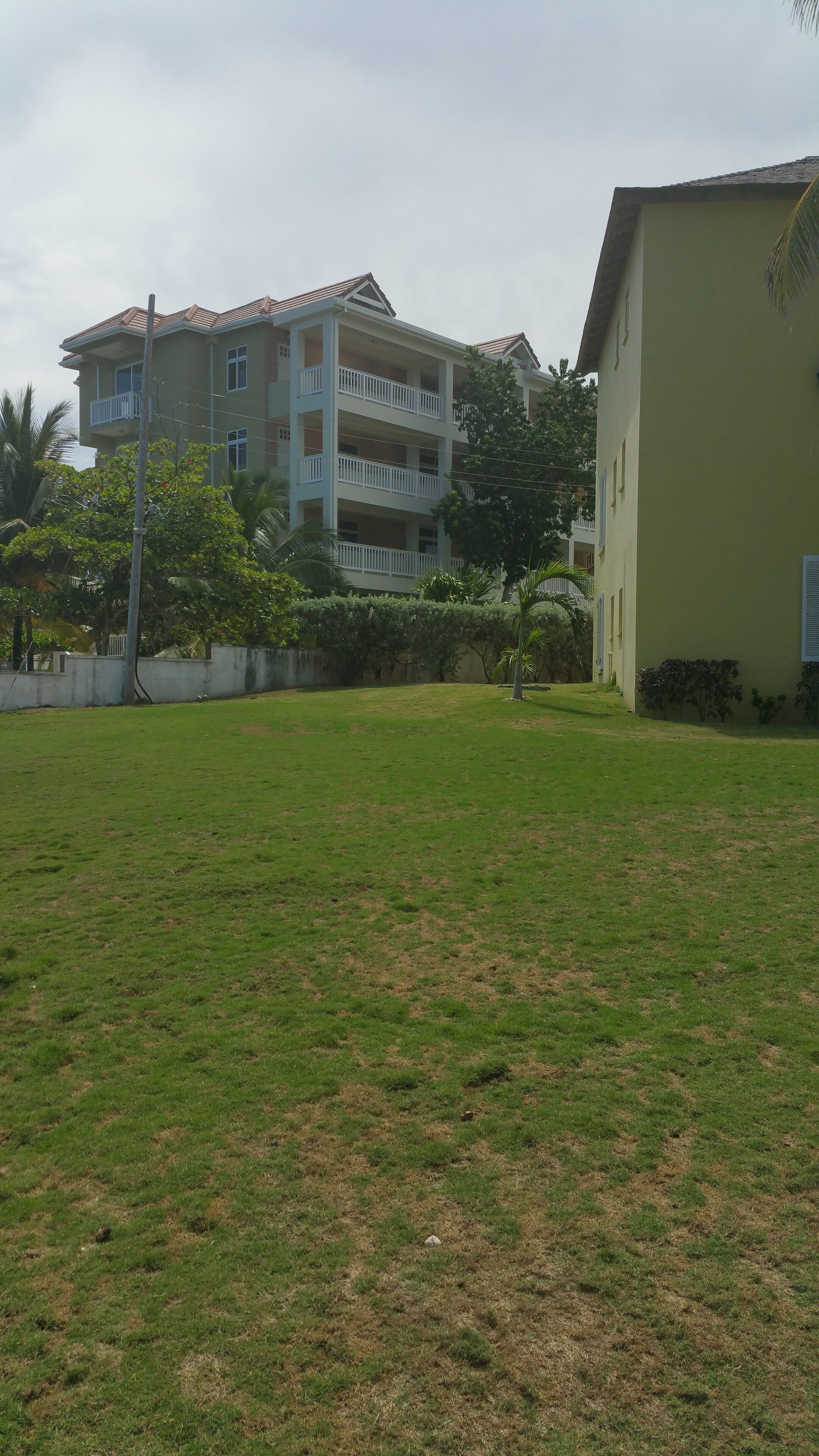 Un immeuble à plusieurs étages doté de balcons, entouré d’une zone herbeuse et d’arbres.