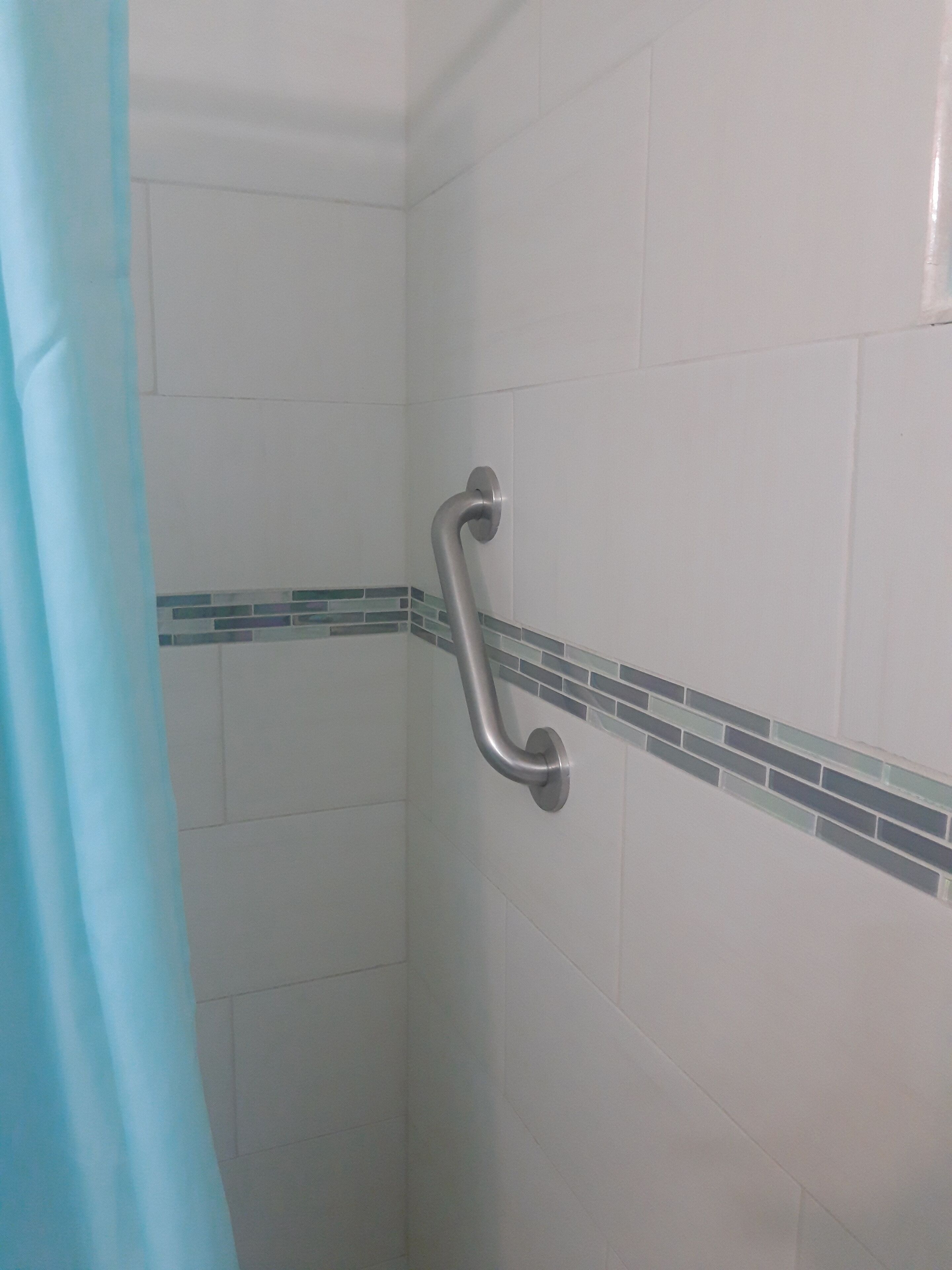 Baño con azulejos blancos, cortina de ducha azul y barra de apoyo.