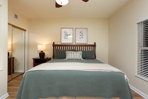 Un dormitorio con una cama, una mesita de noche, una lámpara y dos cuadros colgados en la pared.