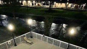 Una piscina de borde curvo, rodeada por una barandilla blanca y un deck pavimentado.