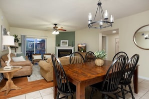 A dining area with a wooden table and chairs, a chandelier, and a fireplace.