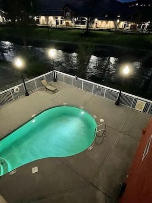 Una piscina con borde curvo, rodeada por una terraza con barandillas y algunas sillas de descanso.