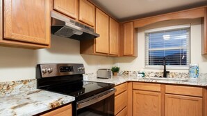Una cocina con armarios de madera, una campana extractora de acero inoxidable, un horno negro, un microondas integrado y una ventana con persianas.