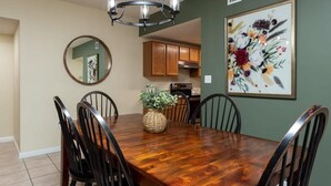 Un comedor con una mesa de madera, sillas negras, una lámpara de araña, un espejo y una obra de arte floral enmarcada en la pared.