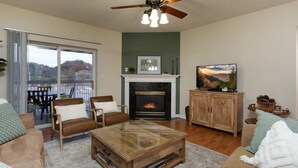 Una sala de estar con chimenea, ventilador de techo y un ventanal con vistas a una terraza.
