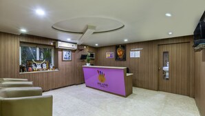Zona de recepción con un mostrador morado, paneles de madera, una lámpara en el techo, una ventana con plantas y un cuadro en la pared.