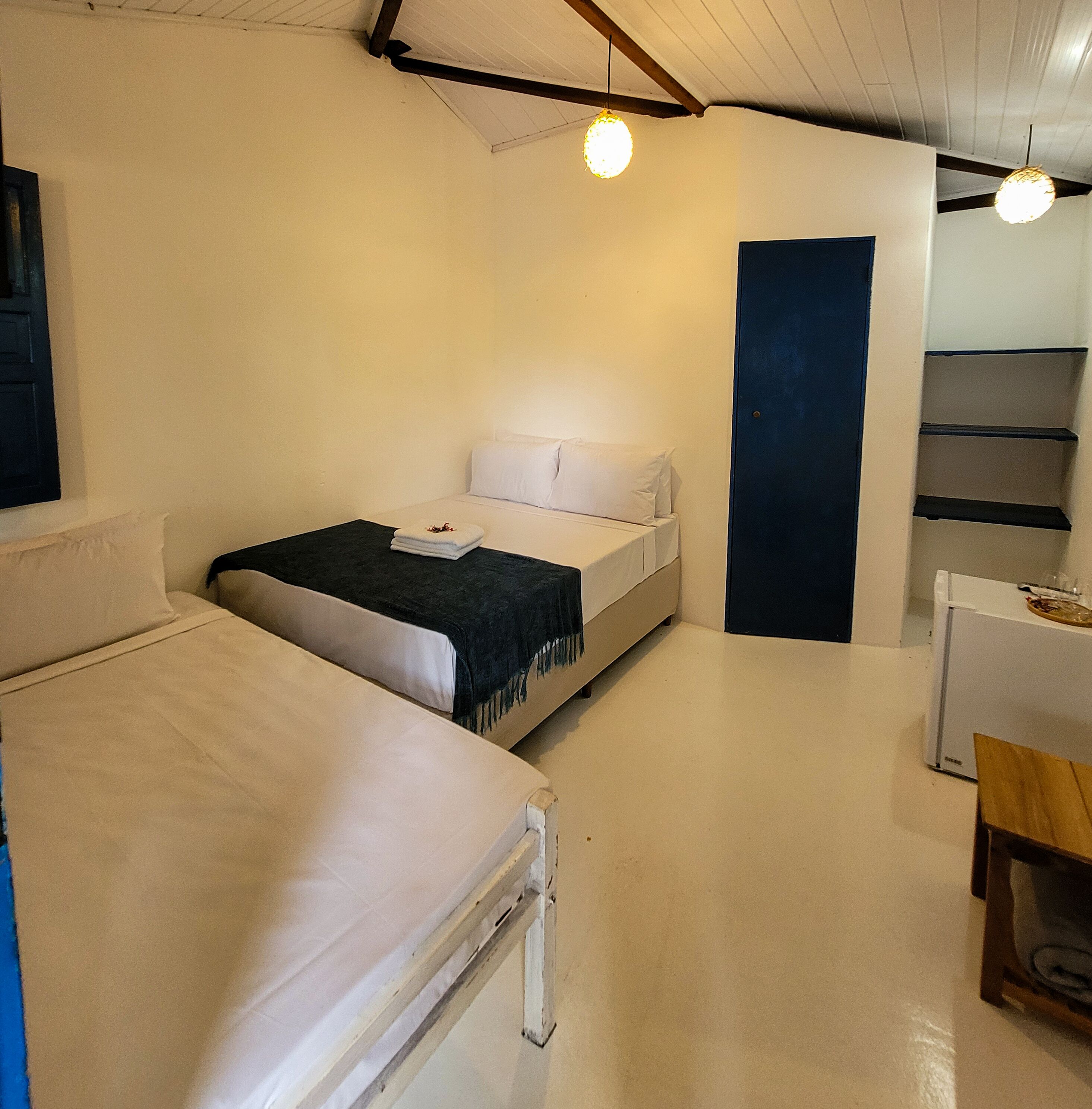 A small, simple room with a bed, a desk, and a chair. There are two light fixtures on the ceiling.