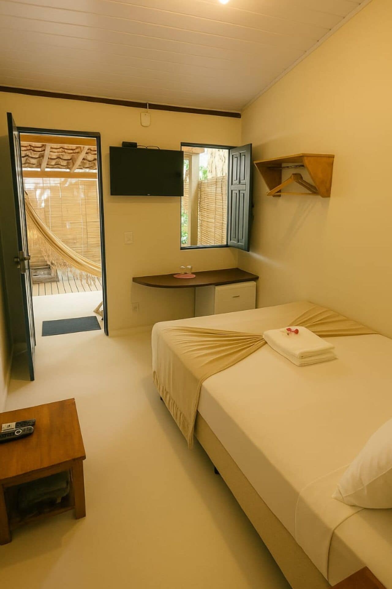 A hotel room with a bed, a small desk, a television, and a window with a view of the outdoors.
