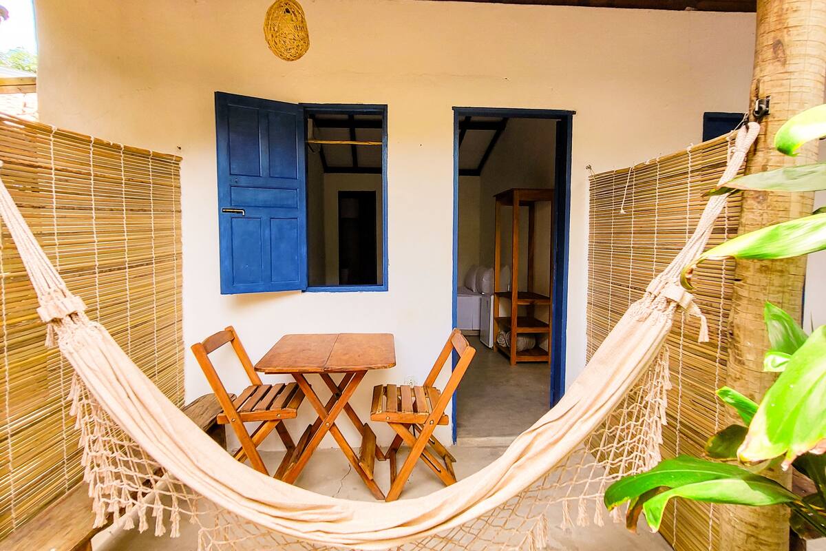 A hammock set up between two bamboo walls with a wooden table and chairs in the center.