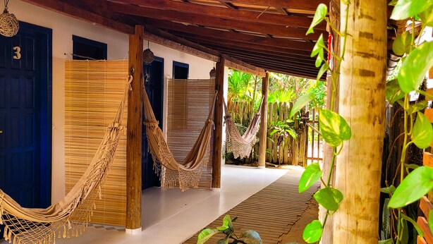 A covered walkway with hammocks, wooden doors, and a tropical garden. - Pousada Vilarejo (Porto Seguro)