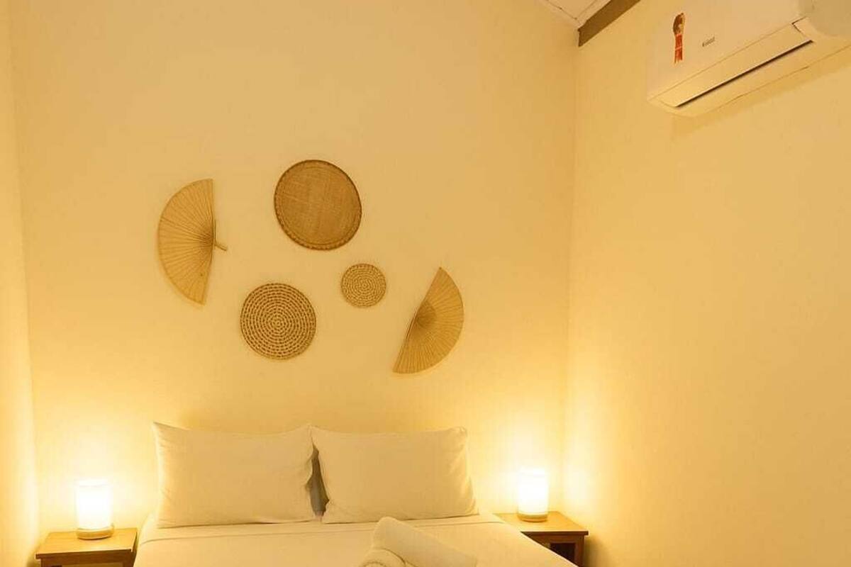 A neatly made bed with a white bedspread, two bedside lamps, and a wall-mounted air conditioner.