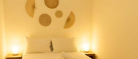 A neatly made bed with a white bedspread, two bedside lamps, and a wall-mounted air conditioner.