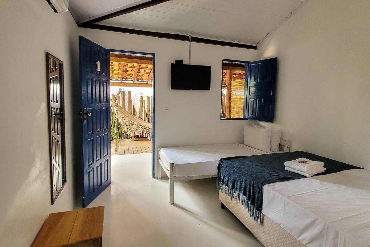 A bedroom with two beds, a wooden table, and a view of a wooden deck through an open door.