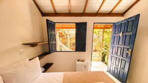 A bedroom with a bed, a small table, a heater, and a window with open shutters. - Pousada Vilarejo (Porto Seguro)