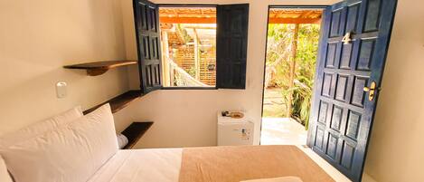 A bedroom with a bed, a small table, a heater, and a window with open shutters.