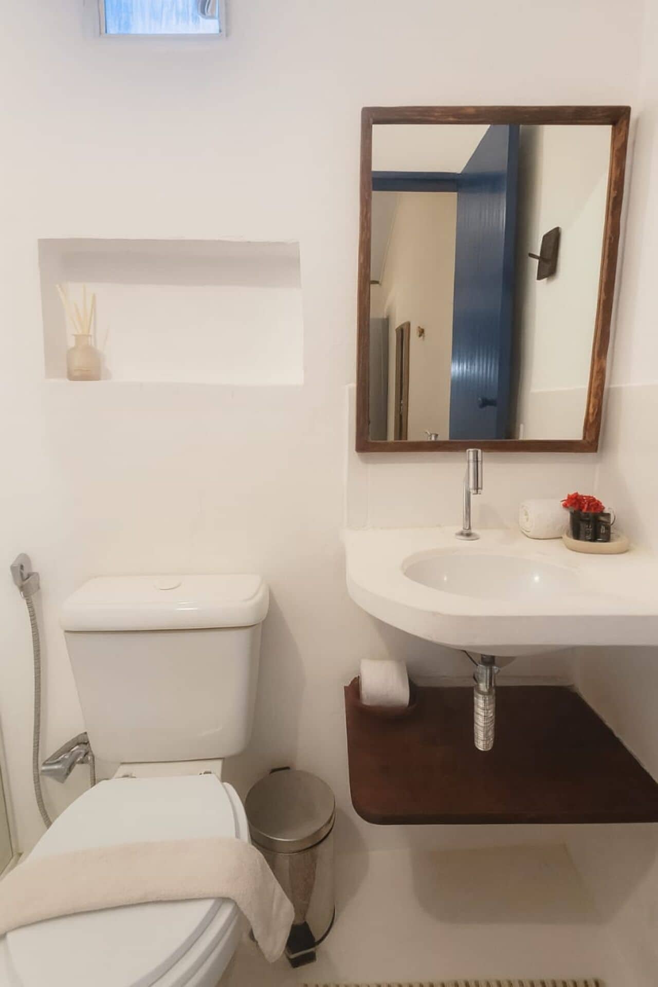 A bathroom with a white toilet, a sink with a mirror above it, and a small shelf above the sink.