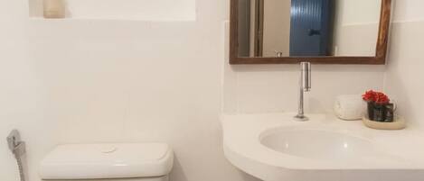 A bathroom with a white toilet, a sink with a mirror above it, and a small shelf above the sink.