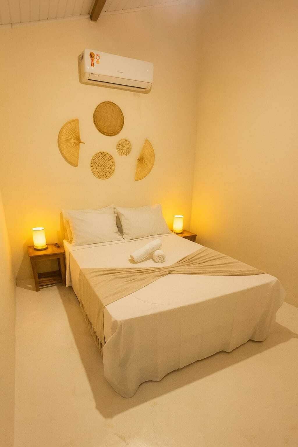 A bedroom with a bed, two bedside tables with lamps, an air conditioning unit, and wall decorations.