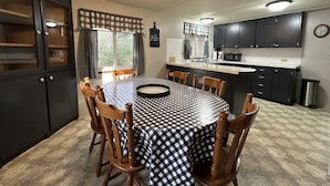 A compact kitchen with dark cabinets, a microwave, and a sink. There is a dining table with a checkered tablecloth and wooden chairs.
