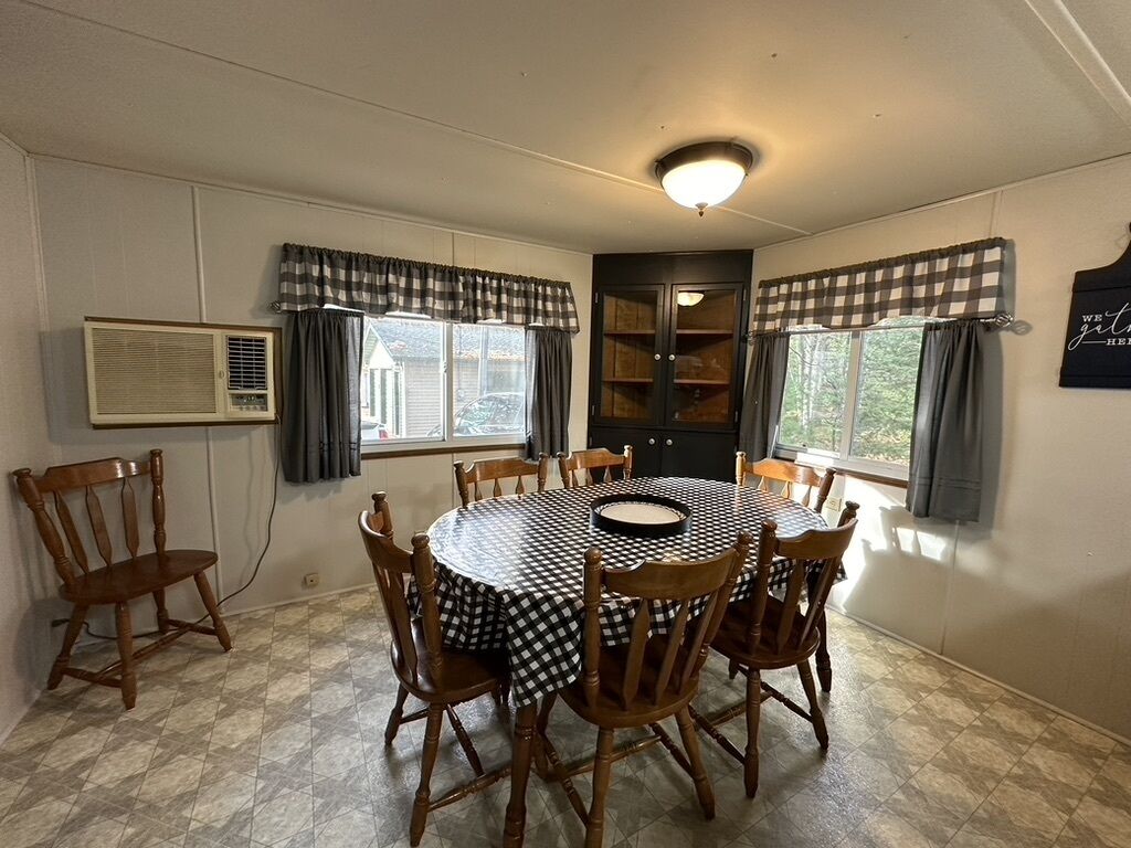 A dining area with a round table, six wooden chairs, checkered tablecloth, and a ceiling light fixture.
