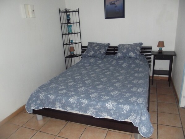 Un dormitorio con cama, mesita de noche, estante y un cuadro en la pared.
