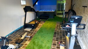 A home gym with a treadmill, stationary bike, and exercise equipment on a tiled floor with artificial grass.