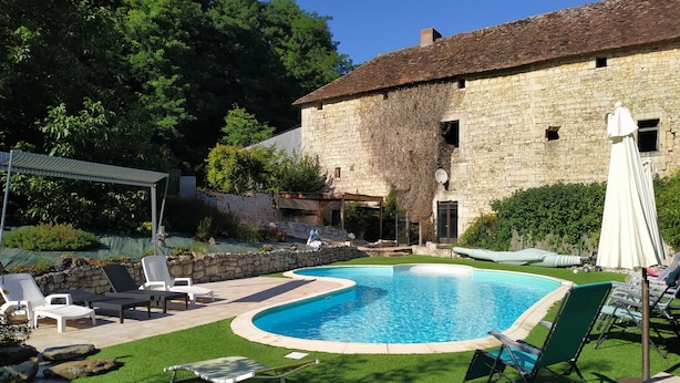 A swimming pool with lounge chairs, a stone building, and a grassy area.
