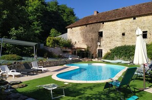 Una piscina con sillas de descanso, un edificio de piedra y un área con césped.