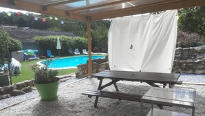 An outdoor patio with a pool, a covered seating area, and a green potted plant.