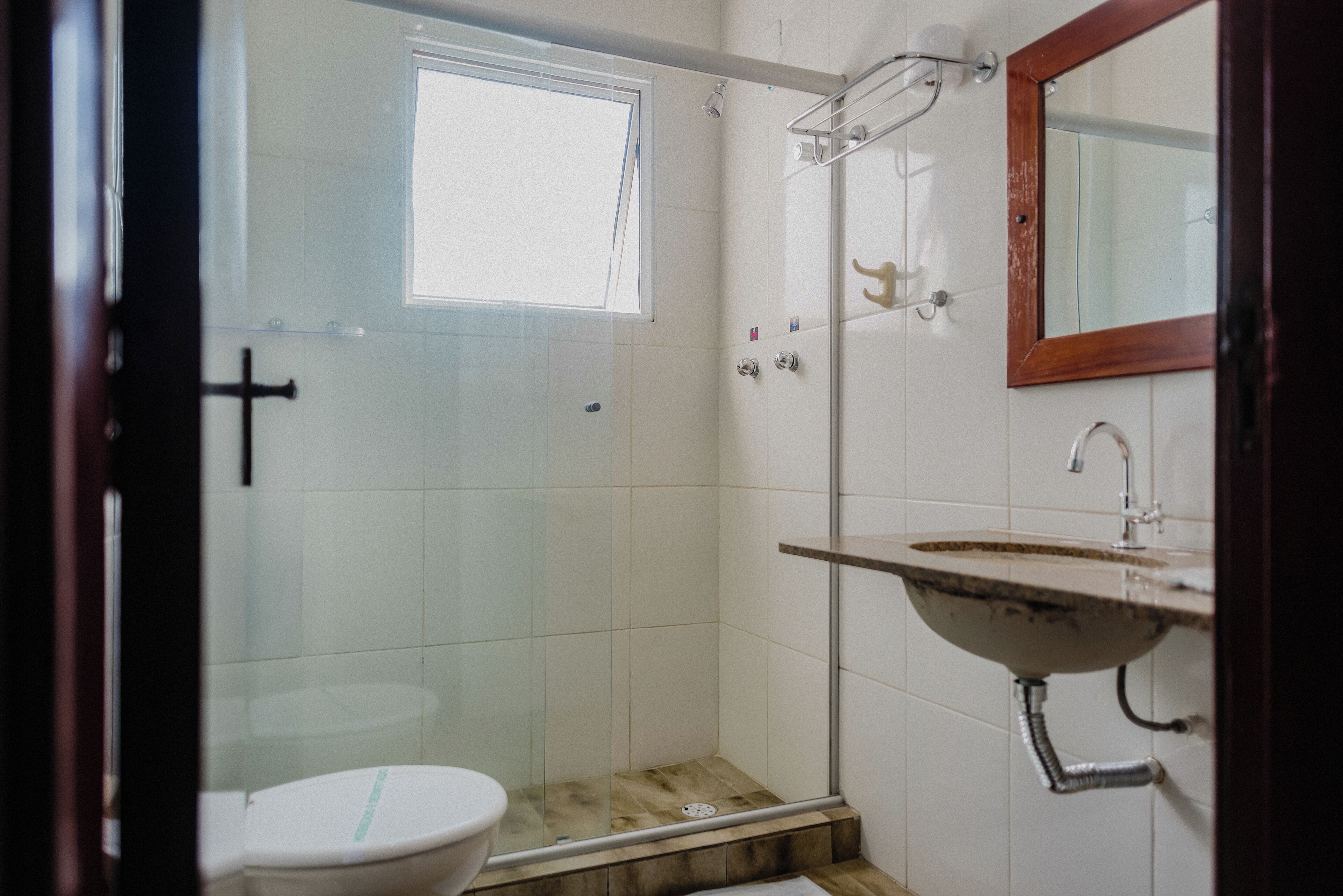 Un baño con ducha envuelta en vidrio, inodoro blanco y lavamanos con encimera de madera.