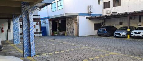 A parking area with hexagonal tiles, a blue and white building with air conditioning units, and several parked cars.