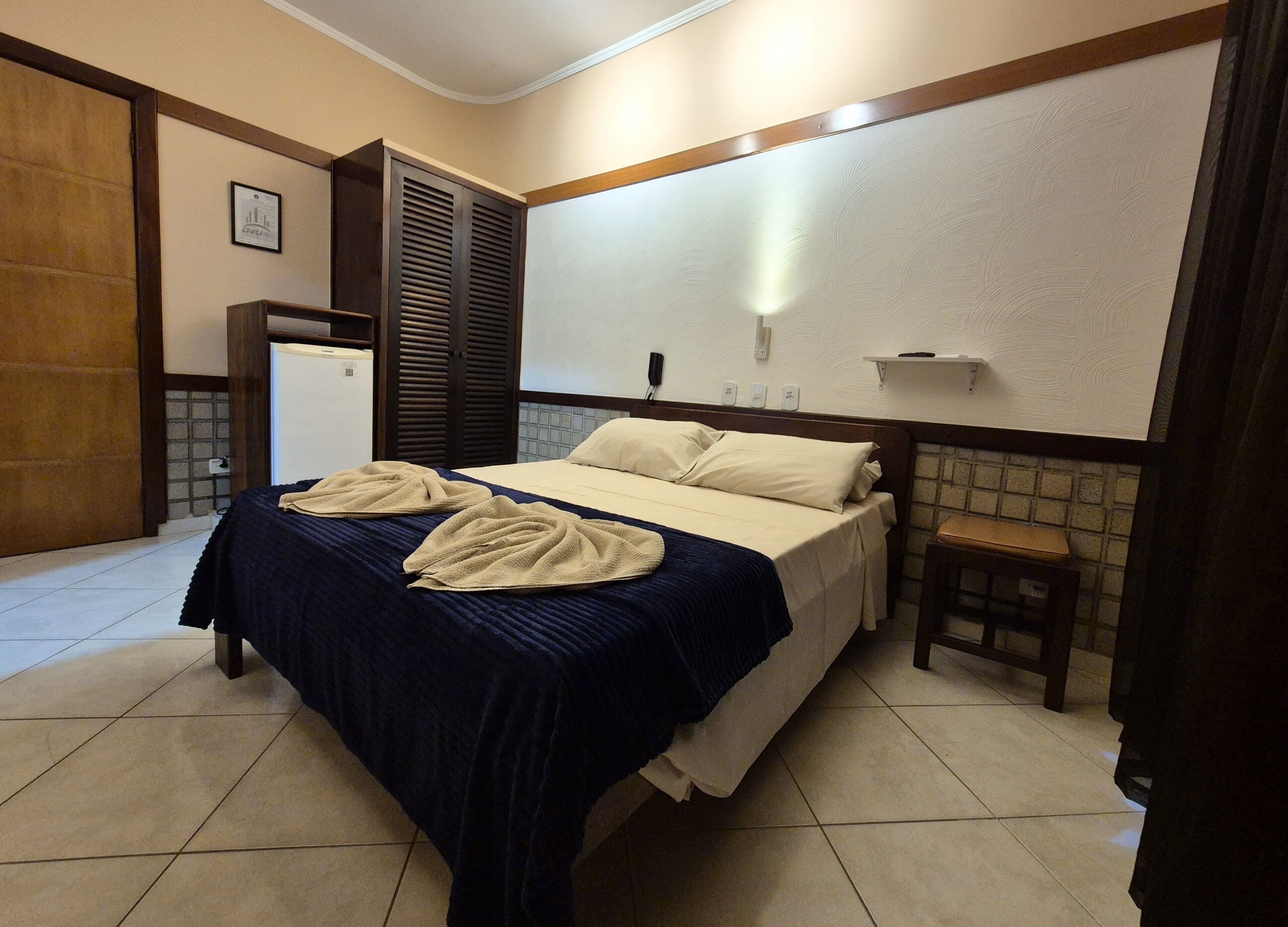 Ein Hotelzimmer mit einem Bett, einem kleinen Tisch, einem an der Wand befestigten Regal und einer Tür.