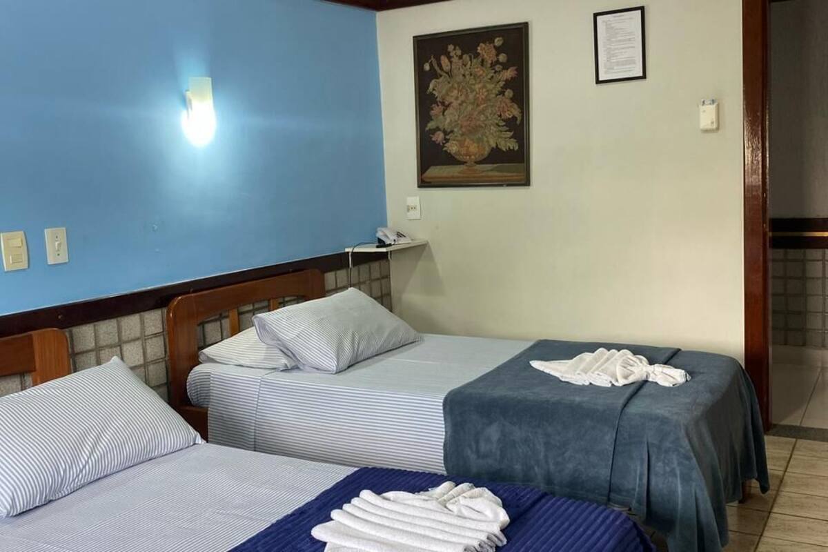 A hotel room with two beds, a painting on the wall, and a door leading to another room.