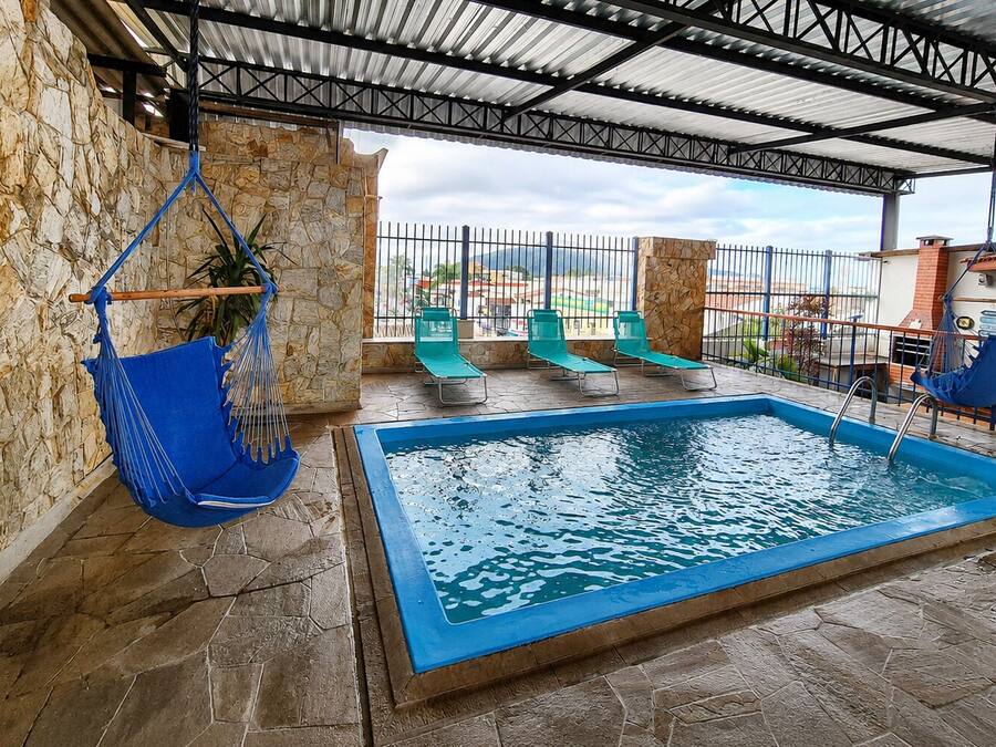 An outdoor swimming pool with stone walls and a metal roof, surrounded by lounge chairs and a hanging chair.
