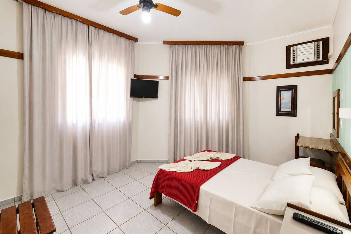 A hotel room with a bed, a ceiling fan, a TV, and a window with curtains.