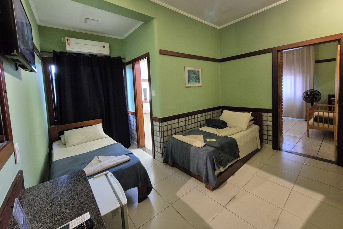 A room with two beds, a television, an air conditioning unit, and a fan.