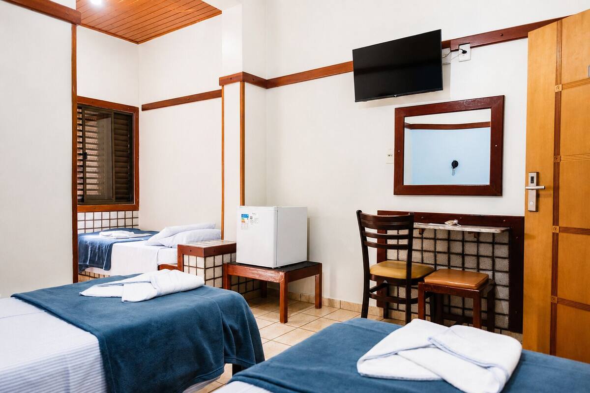 A hotel room with two beds, a television, a mirror, a refrigerator, and a wooden chair.