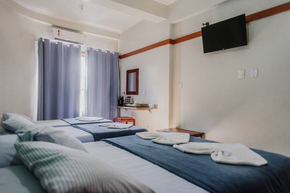 A hotel room with two beds, a TV mounted on the wall, and a window with curtains.