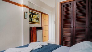 Ein Hotelzimmer mit einem Bett, einem Holzschrank, einem Bild an der Wand und einer Tür mit Klappläden.