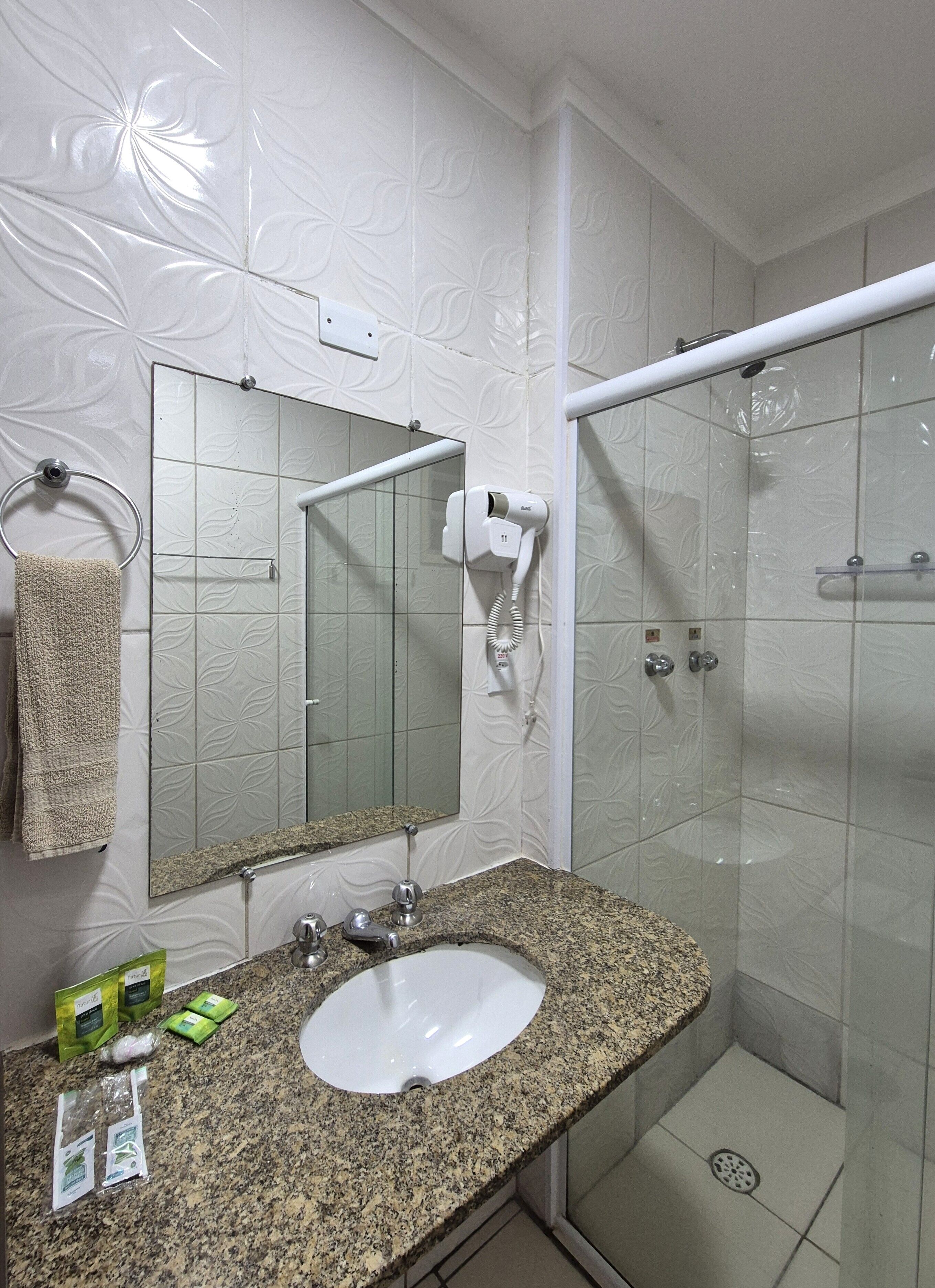 Casa de banho com bancada em granito, um suporte para toalhas, espelho, secador de cabelo e cabine de duche.