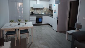 Eine moderne Küche mit weißen Schränken, einer Mikrowelle, einem Herd und einem Kühlschrank. Ein Esstisch mit Stühlen und zwei Zimmerpflanzen sind ebenfalls vorhanden.