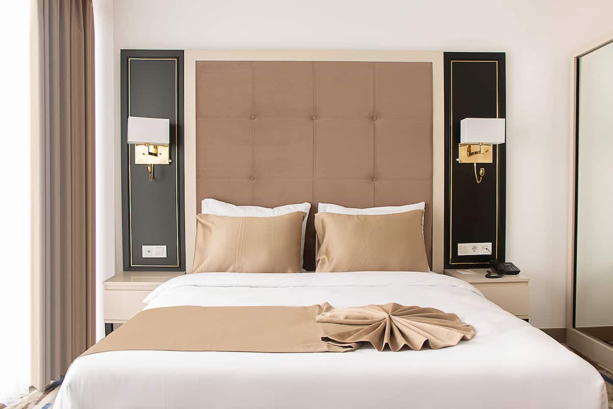 Quarto de hotel com uma cama grande, duas mesas de cabeceira, encosto de cama e luminárias fixadas na parede.