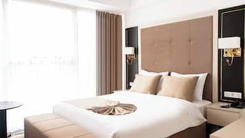 A hotel room with a bed, bedside table, lamp, and a view of the outside.